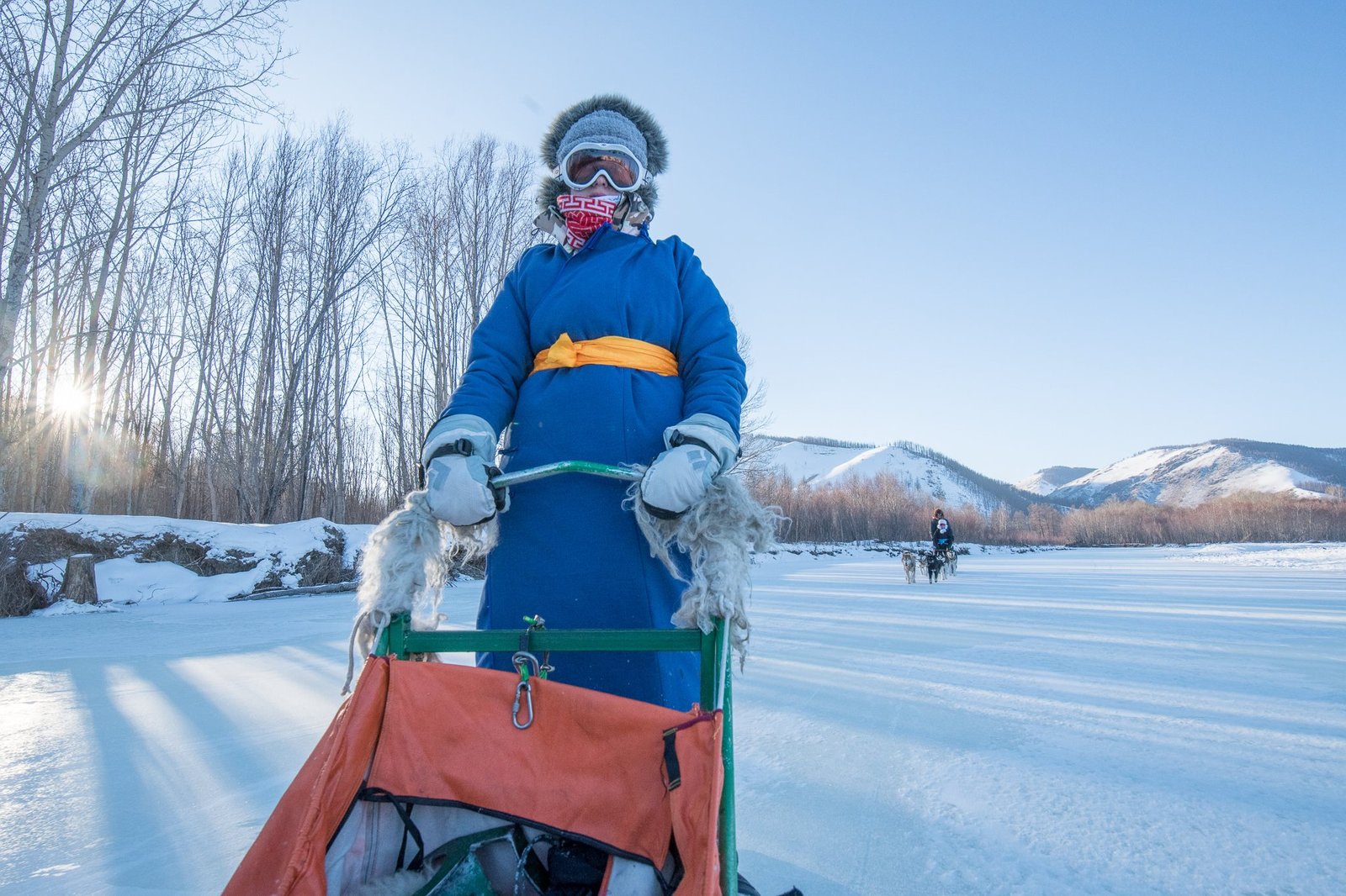 A person wearing a traditional Mongolian del while dog sledding in Mongolia