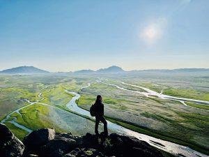 Pujee - a trip assistant with Eternal Landscapes - achieving new heights standing on top of a mountain overlooking a river.
